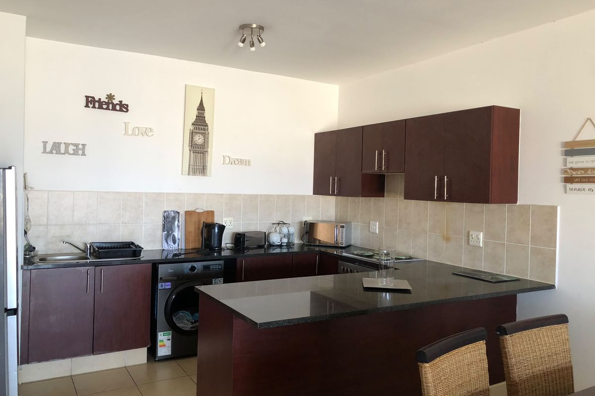 Functional kitchen featuring dark wood cabinetry, granite countertops, tiled backsplash, and an integrated washing machine, offering a practical layout for daily use.