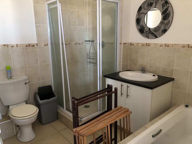 A functional bathroom featuring a shower enclosure, bathtub, vanity cabinet with basin, and toilet, finished with neutral wall and floor tiling.