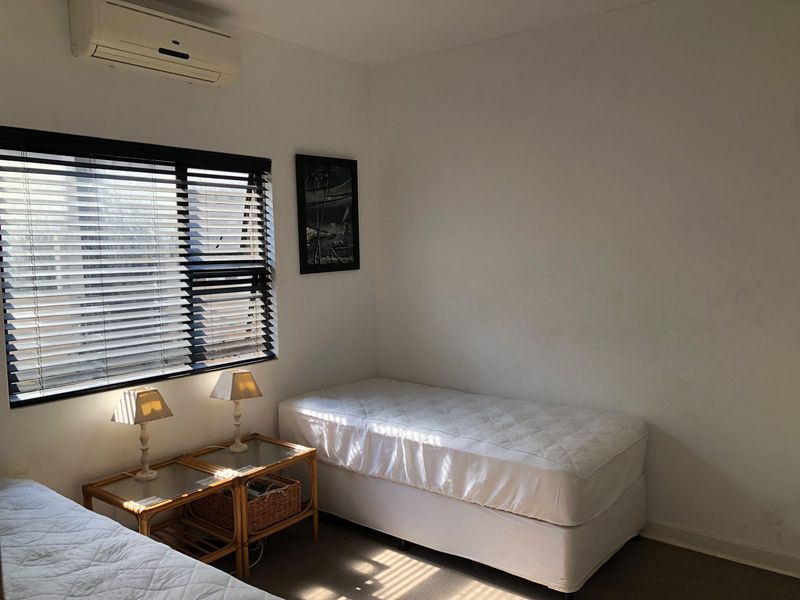 A functional bedroom featuring a wall-mounted split-system air conditioner and venetian blinds, providing a neutral space ready for personalization.