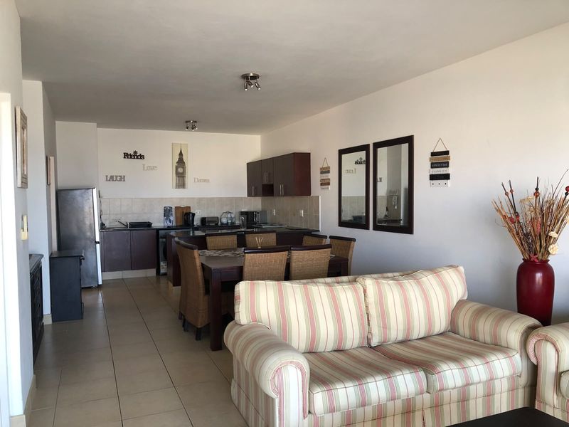 Open plan living and dining area featuring tiled floors and a functional kitchen with built-in cabinetry and a tiled backsplash.
