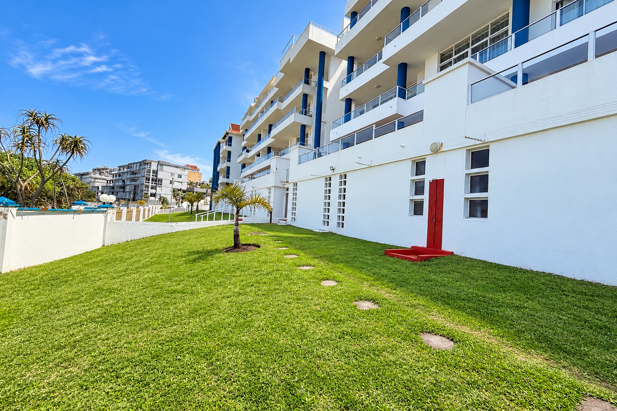 A well-maintained rear exterior view of the apartment complex featuring a landscaped lawn, stone pathway, and an outdoor shower facility.