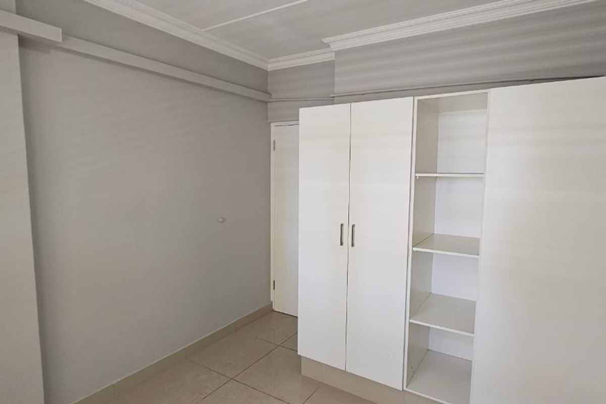 A clean, empty bedroom featuring neutral wall tones, tiled flooring, crown molding, and a functional built-in wardrobe with shelving.
