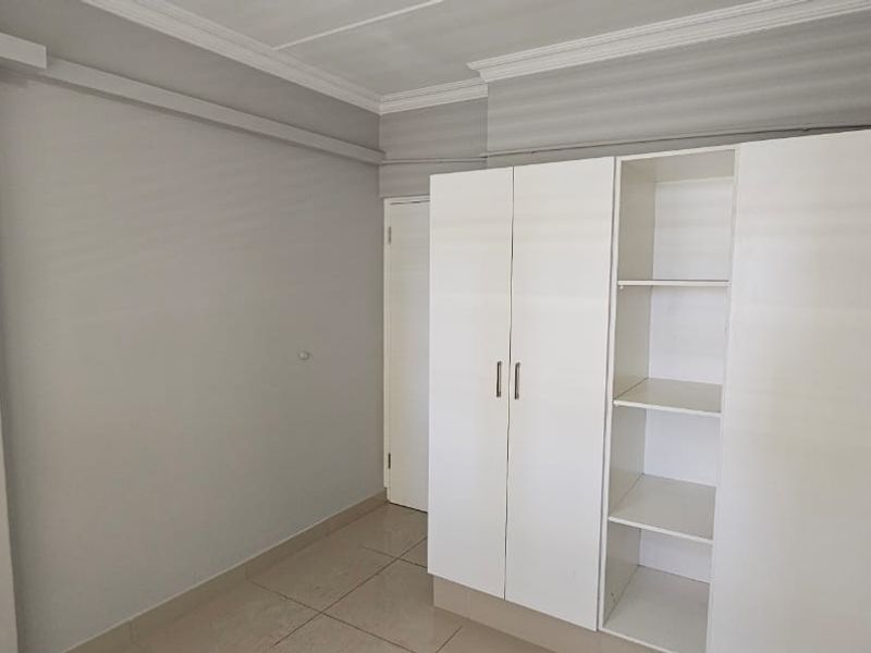 A clean, empty bedroom featuring neutral wall tones, tiled flooring, crown molding, and a functional built-in wardrobe with shelving.