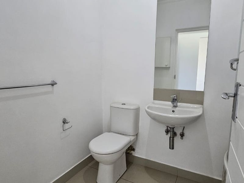 A clean and functional guest bathroom featuring a wall-mounted basin, toilet, and neutral tiled flooring.