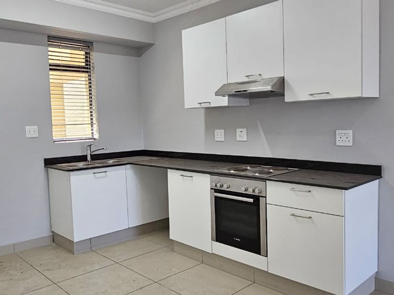 A clean, modern kitchen featuring white cabinetry, dark countertops, built-in oven, electric hob, extractor fan, and tiled flooring.