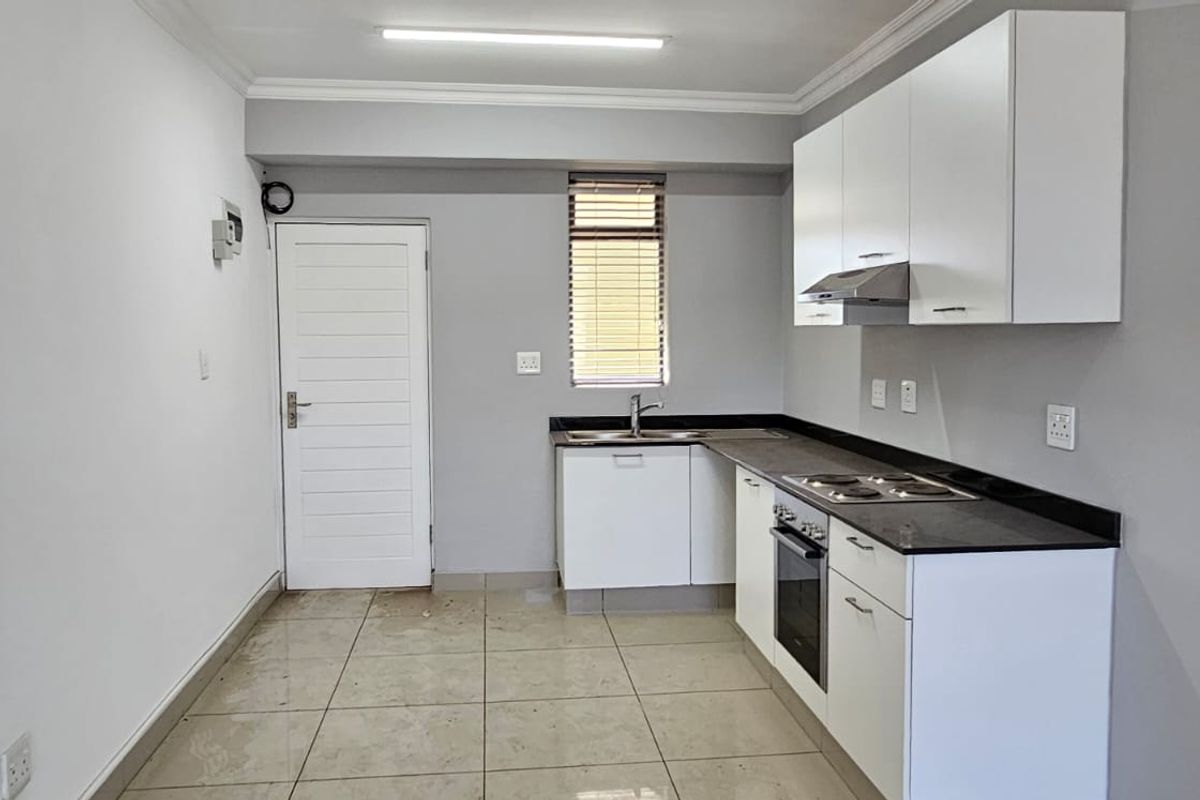 A clean, functional kitchen featuring white cabinetry, dark stone countertops, built-in oven, hob, and extractor fan with tiled flooring.