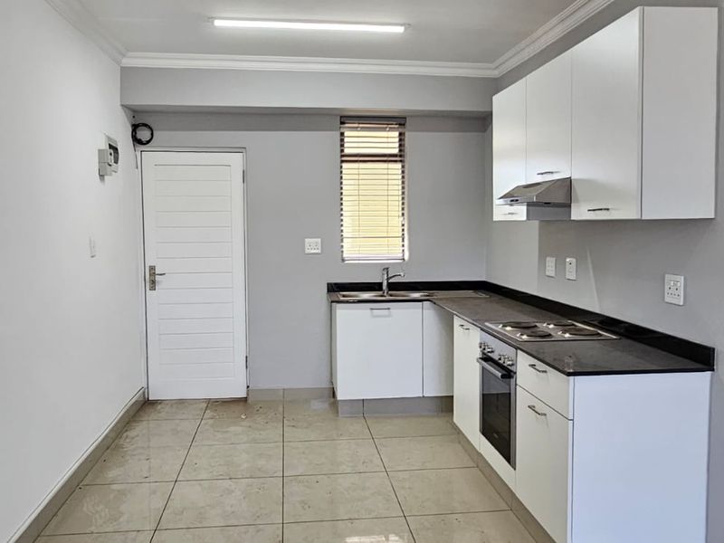 A clean, functional kitchen featuring white cabinetry, dark stone countertops, built-in oven, hob, and extractor fan with tiled flooring.