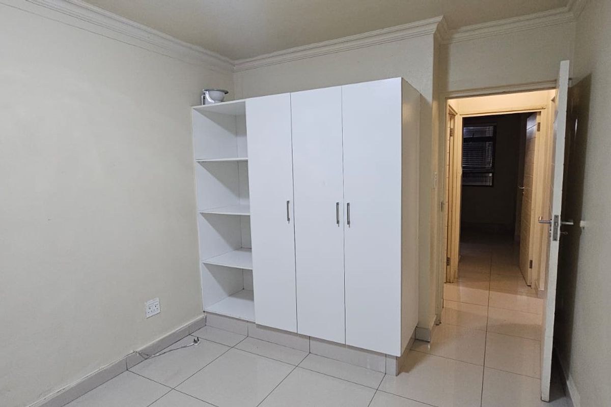 A clean, empty bedroom featuring neutral tiled flooring, crown molding, and a white built-in wardrobe with open shelving.
