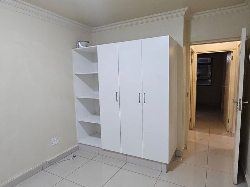 A clean, empty bedroom featuring neutral tiled flooring, crown molding, and a white built-in wardrobe with open shelving.