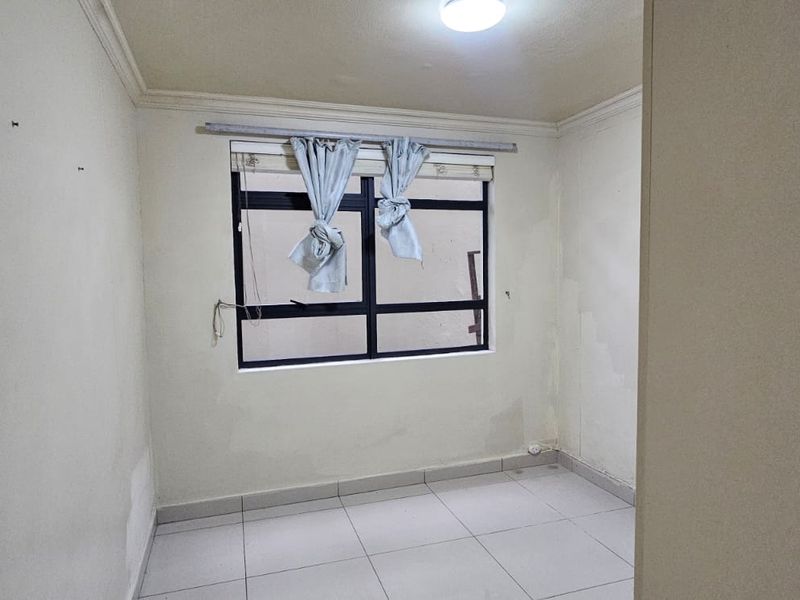 An empty bedroom featuring tiled flooring and an aluminium window frame, requiring minor cosmetic updates to the wall finishes.