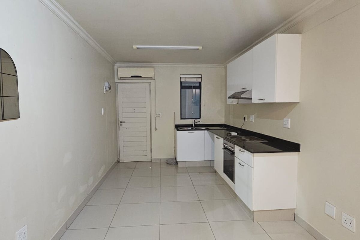A functional, empty kitchen featuring white cabinetry, dark stone countertops, integrated oven, extractor fan, and tiled flooring with an installed air conditioning unit.