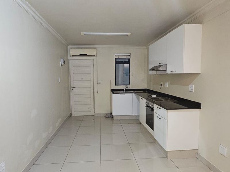 A functional, empty kitchen featuring white cabinetry, dark stone countertops, integrated oven, extractor fan, and tiled flooring with an installed air conditioning unit.