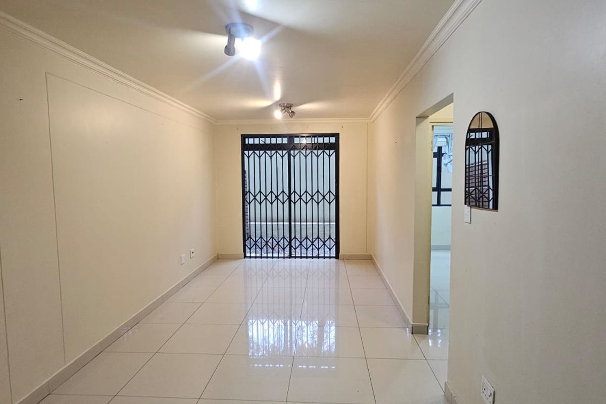 A bright, empty living area featuring neutral tiled flooring, ceiling cornices, and a secure metal gate leading to an outdoor space.