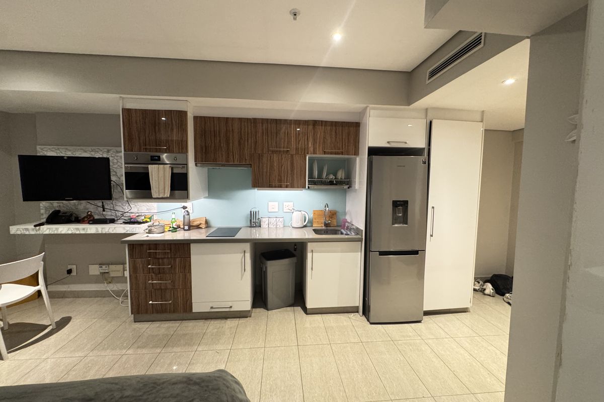 Modern kitchen featuring two-tone cabinetry, integrated appliances, glass splashback, and tiled flooring, seamlessly integrated into an open-plan living space.