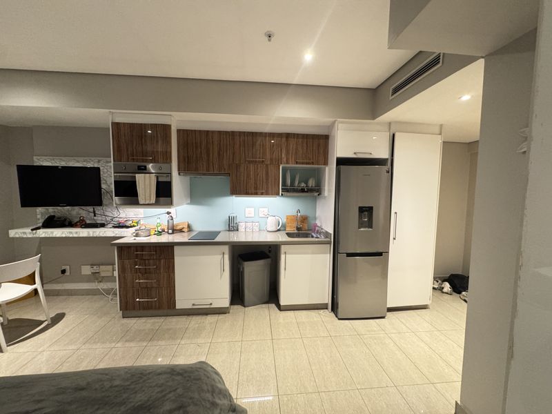 Modern kitchen featuring two-tone cabinetry, integrated appliances, glass splashback, and tiled flooring, seamlessly integrated into an open-plan living space.