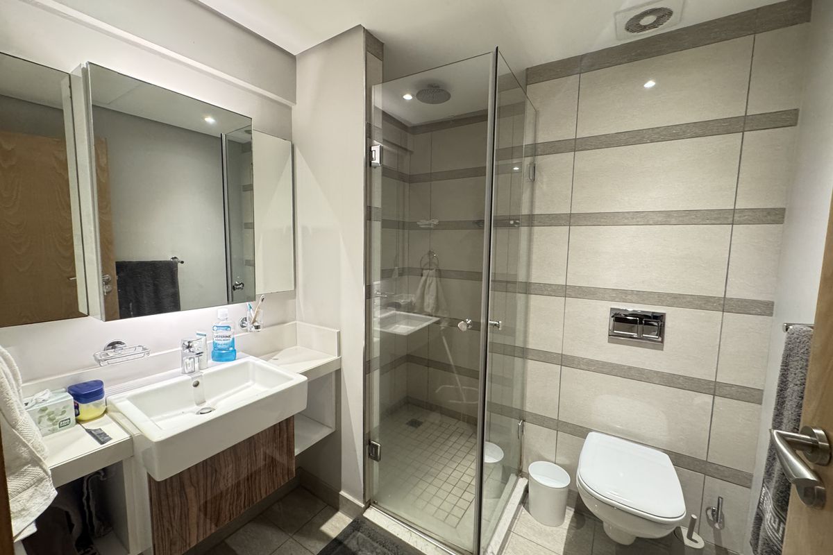 Modern bathroom featuring a wall-mounted vanity with integrated basin, a glass-enclosed shower, and a wall-hung toilet with contemporary tiled finishes.