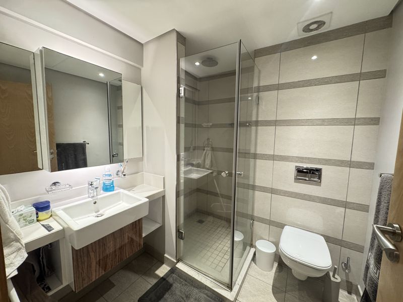 Modern bathroom featuring a wall-mounted vanity with integrated basin, a glass-enclosed shower, and a wall-hung toilet with contemporary tiled finishes.