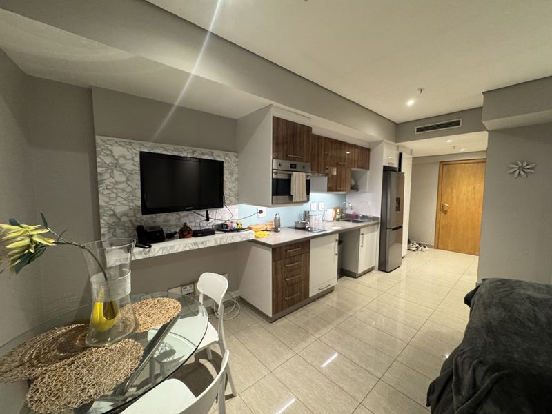 Modern open-plan apartment living area featuring a compact kitchen with built-in cabinetry, integrated appliances, and sleek tiled flooring throughout.