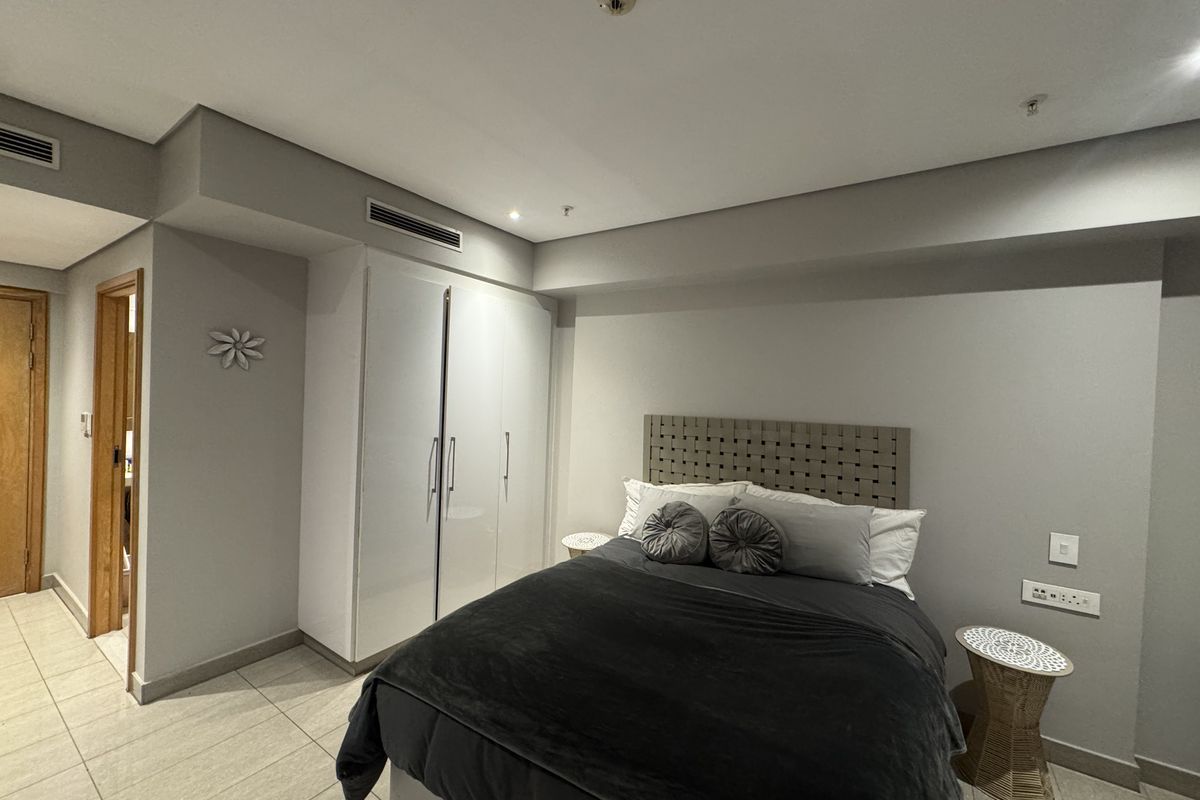 A modern bedroom featuring built-in cupboards, tiled flooring, and integrated ducted air conditioning, offering a clean and functional living space.