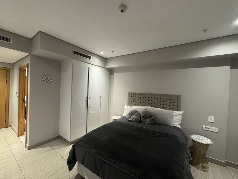 A modern bedroom featuring built-in cupboards, tiled flooring, and integrated ducted air conditioning, offering a clean and functional living space.