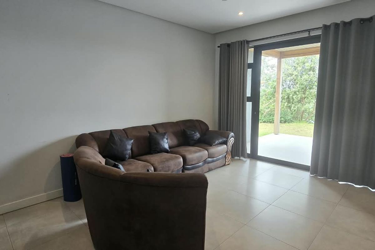 A bright living room featuring large format floor tiles, recessed lighting, and a sliding glass door providing direct access to the outdoor patio area.