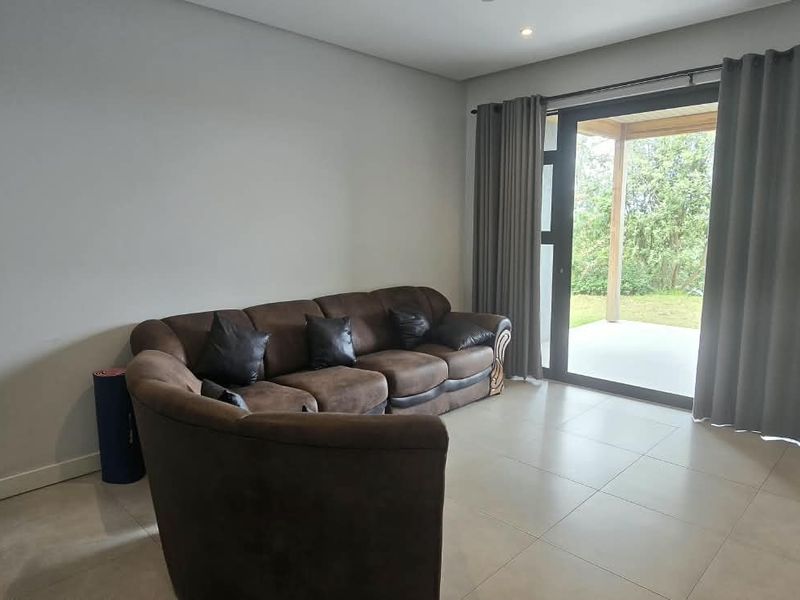 A bright living room featuring large format floor tiles, recessed lighting, and a sliding glass door providing direct access to the outdoor patio area.