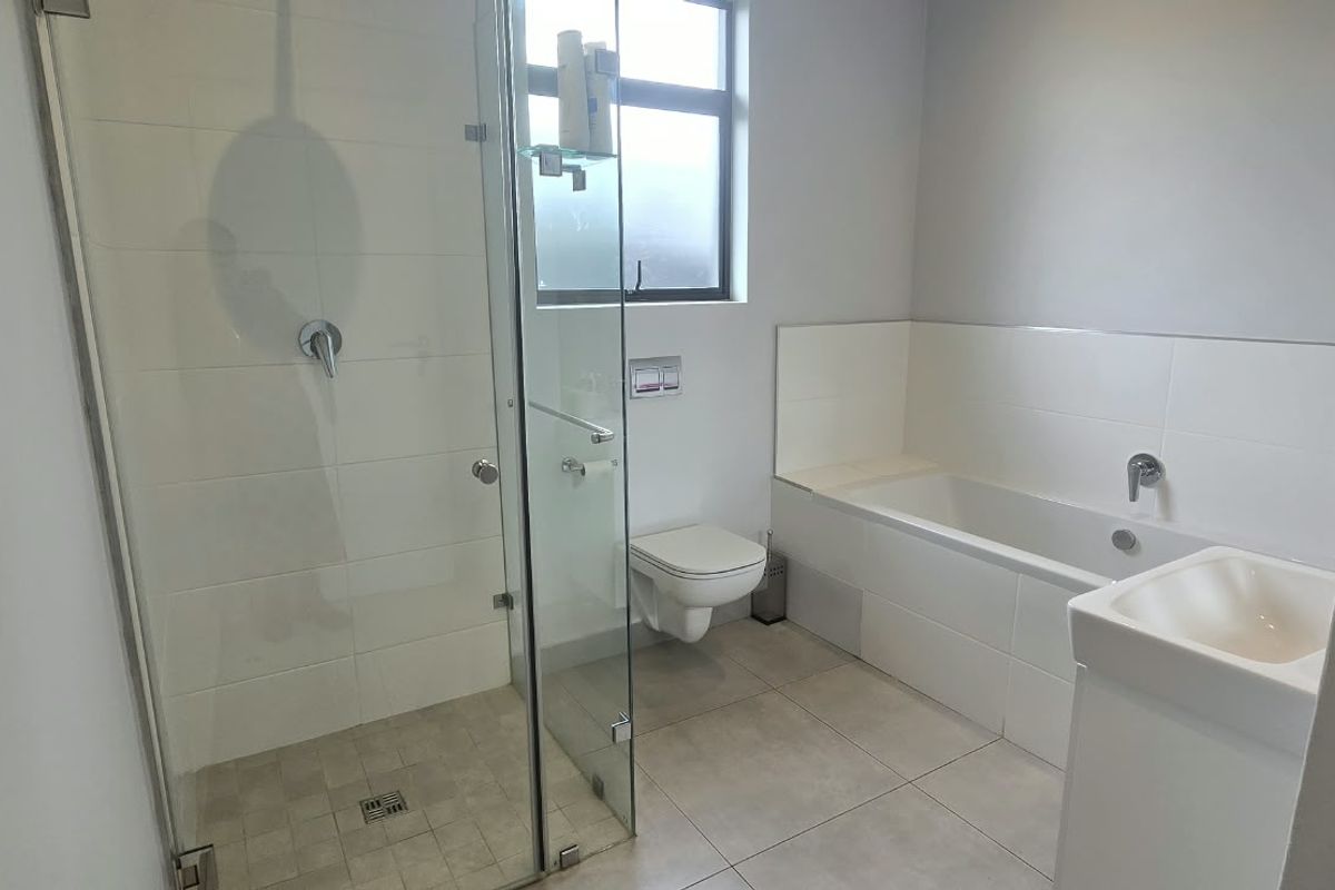 Modern bathroom featuring a glass-enclosed shower, wall-mounted toilet, built-in bathtub, and a vanity basin with neutral tiled finishes.