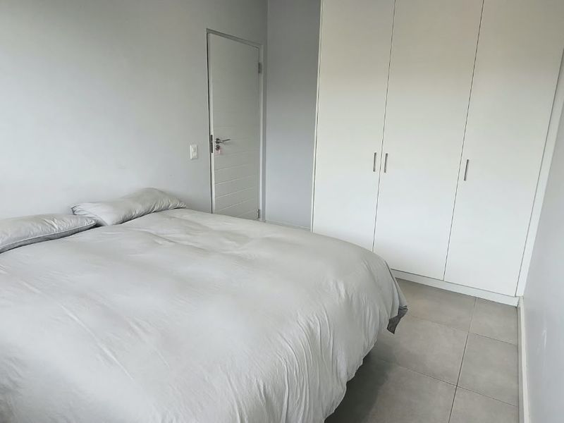 A clean and simple bedroom featuring neutral tiled flooring and ample built-in cupboard storage space.