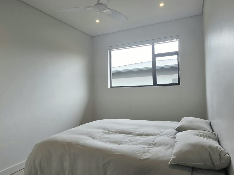 A clean and modern bedroom featuring neutral walls, recessed ceiling lighting, a ceiling fan, and an aluminium-framed window.