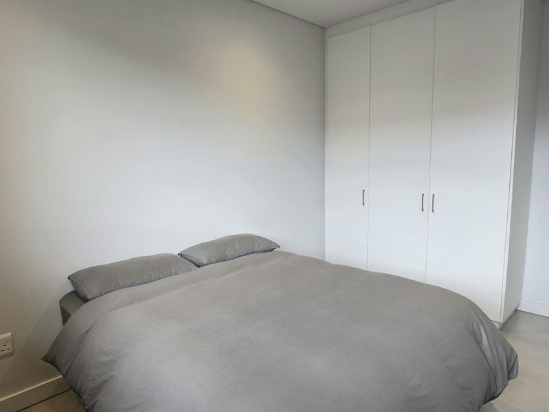 A clean, modern bedroom featuring neutral walls, tiled flooring, and ample built-in cupboard storage.