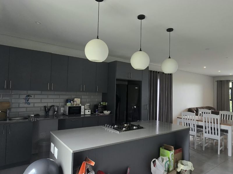 Modern open-plan kitchen and living area featuring dark cabinetry, a central island with a gas hob, tiled floors, and large sliding doors to the patio.