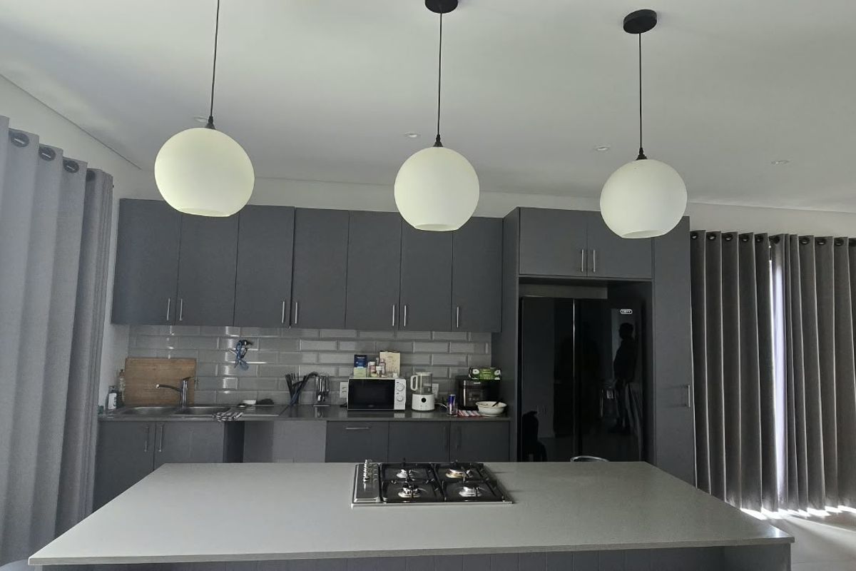 Modern kitchen featuring grey cabinetry, a central island with a built-in gas hob, subway tile backsplash, and contemporary pendant lighting.