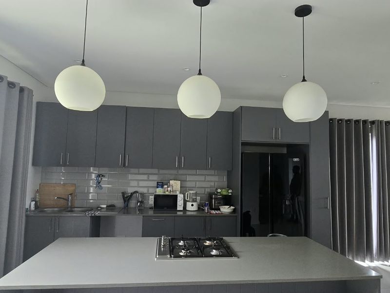 Modern kitchen featuring grey cabinetry, a central island with a built-in gas hob, subway tile backsplash, and contemporary pendant lighting.
