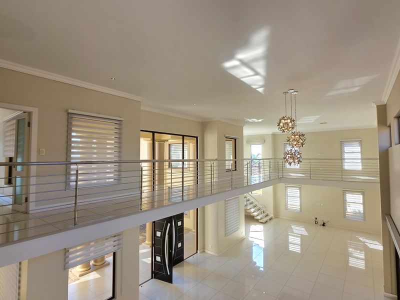 Spacious open-plan double-volume living area featuring sleek tiled floors, modern stainless steel balustrades, and elegant pendant lighting, offering a bright and airy atmosphere.