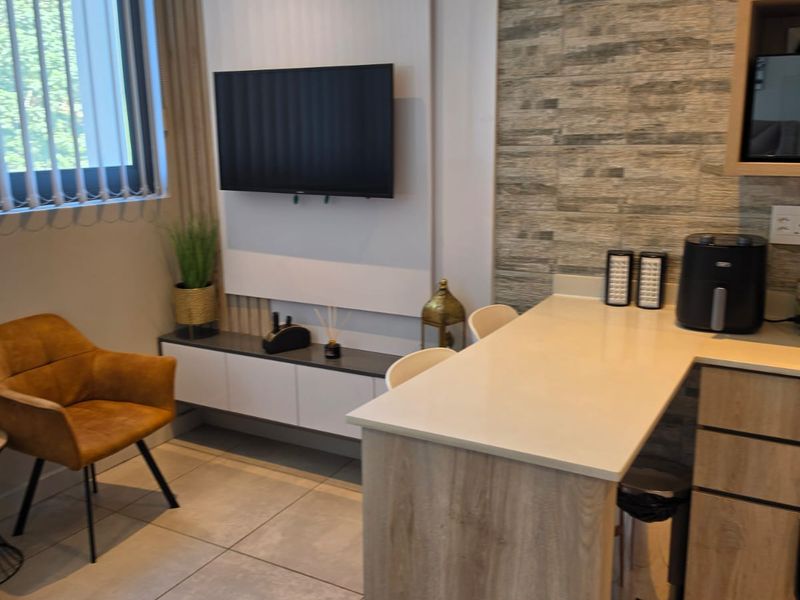Modern open-plan living area featuring a stone-look feature wall, built-in media cabinetry, and a functional breakfast bar with tiled flooring throughout.