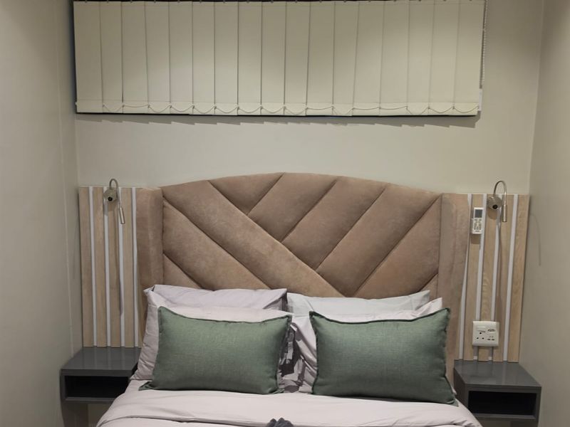 A well-appointed bedroom featuring a custom built-in headboard with integrated bedside tables, wall-mounted lighting, and vertical window blinds.