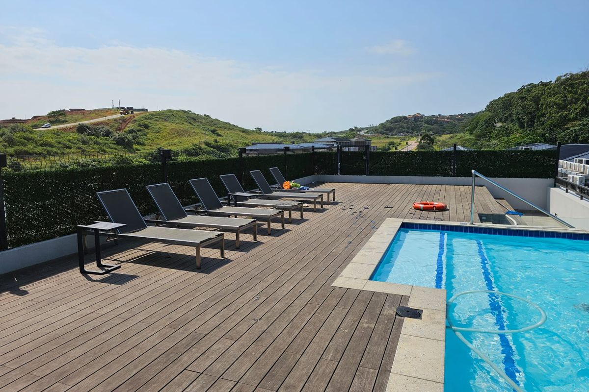 Outdoor pool area featuring timber decking, a swimming pool with coping, and perimeter fencing, offering scenic views of the surrounding landscape.