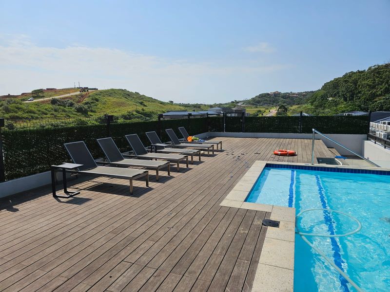 Outdoor pool area featuring timber decking, a swimming pool with coping, and perimeter fencing, offering scenic views of the surrounding landscape.