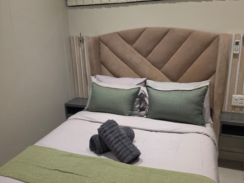 A well-maintained bedroom featuring a custom built-in headboard with integrated bedside tables, vertical blinds, and neutral wall finishes.