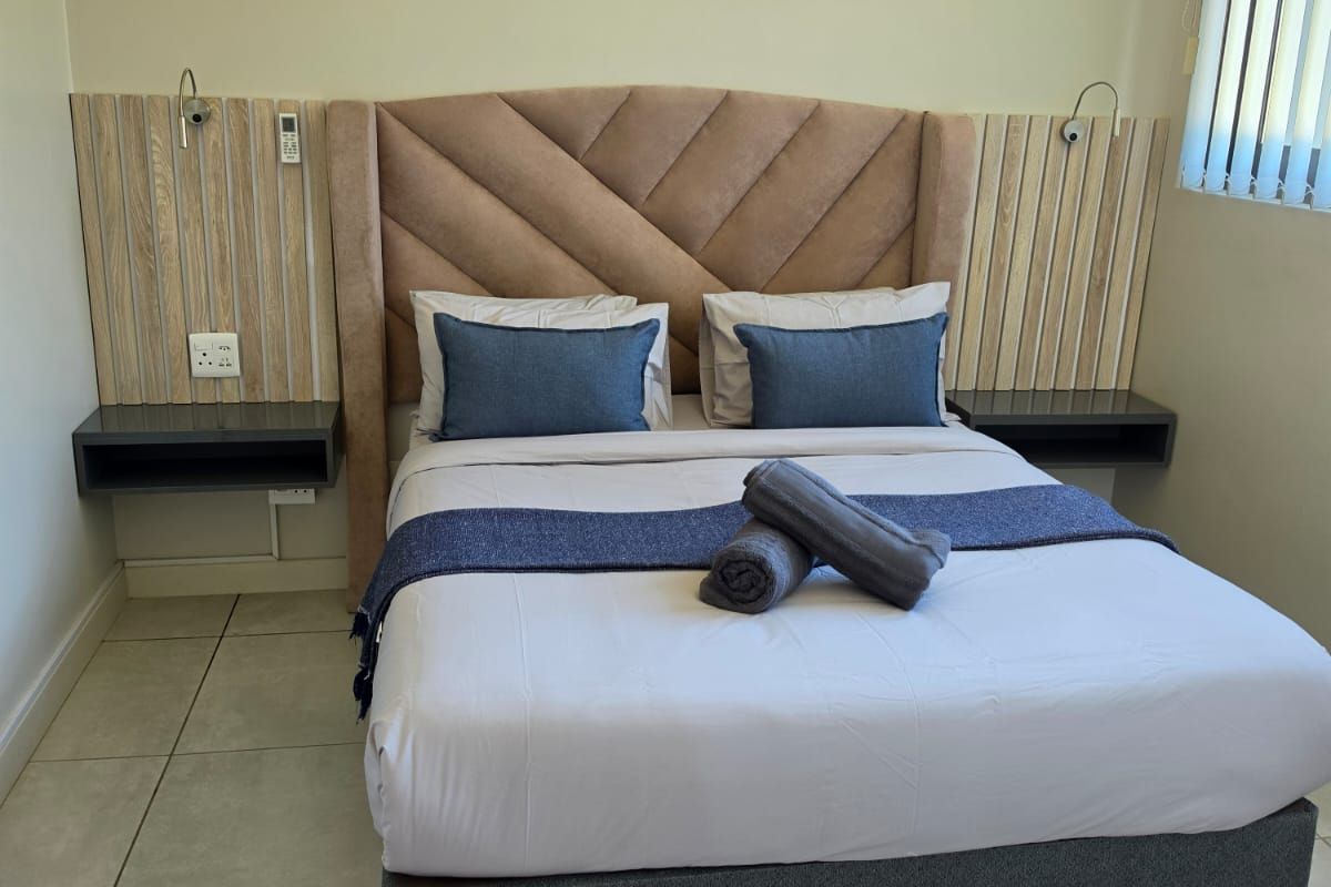 A well-maintained bedroom featuring a custom built-in headboard with integrated floating bedside tables, vertical slat wall paneling, and neutral tiled flooring.