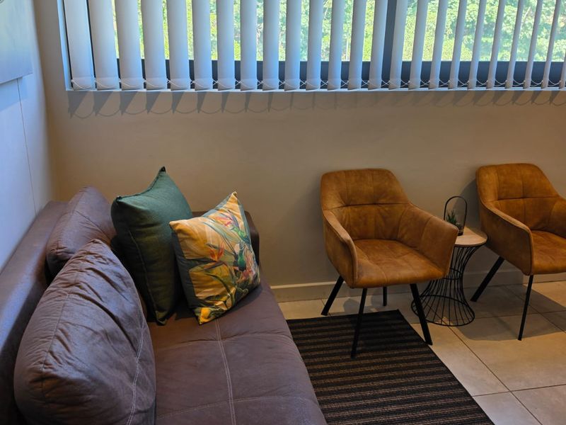 A comfortable living area featuring tiled flooring and large windows fitted with vertical blinds, providing ample natural light.