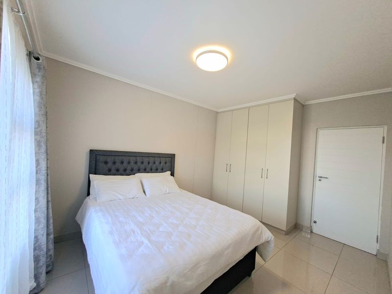 A well-maintained bedroom featuring neutral tiled flooring, built-in wardrobes, and a clean, modern aesthetic with ample natural light.