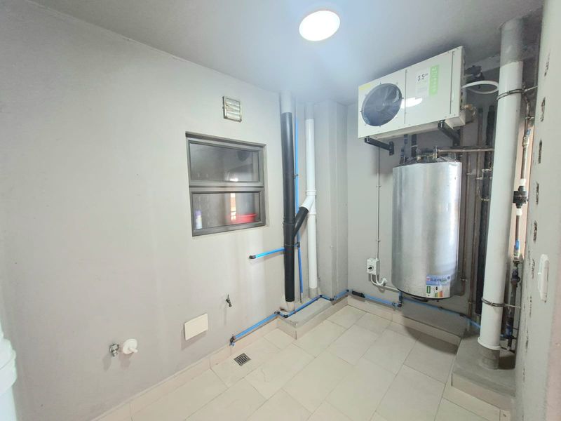 A functional utility space featuring a water heater, air conditioning unit, and exposed plumbing infrastructure with tiled flooring.