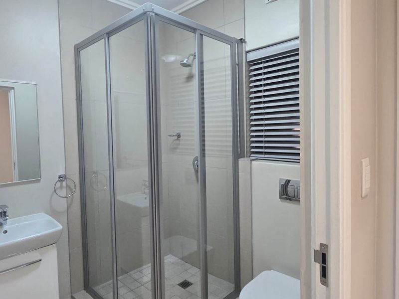 A clean and modern bathroom featuring a glass shower enclosure, wall-mounted basin, and a concealed cistern toilet with neutral tiled finishes.