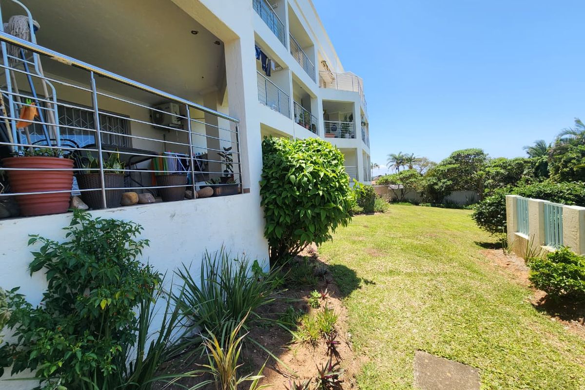 Rear view of the apartment building showing private balconies with stainless steel railings overlooking a shared garden area.