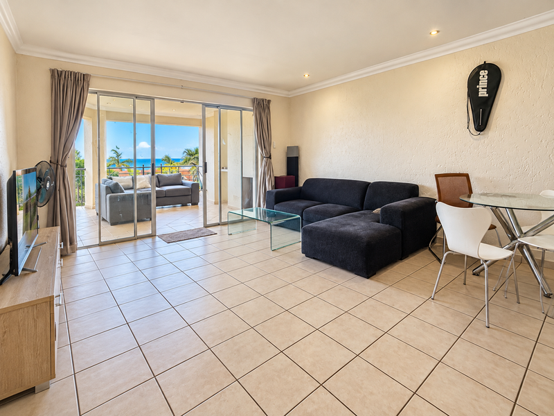 Open-plan living and dining area featuring neutral tiled flooring, recessed lighting, and large sliding glass doors leading to a balcony with ocean views.