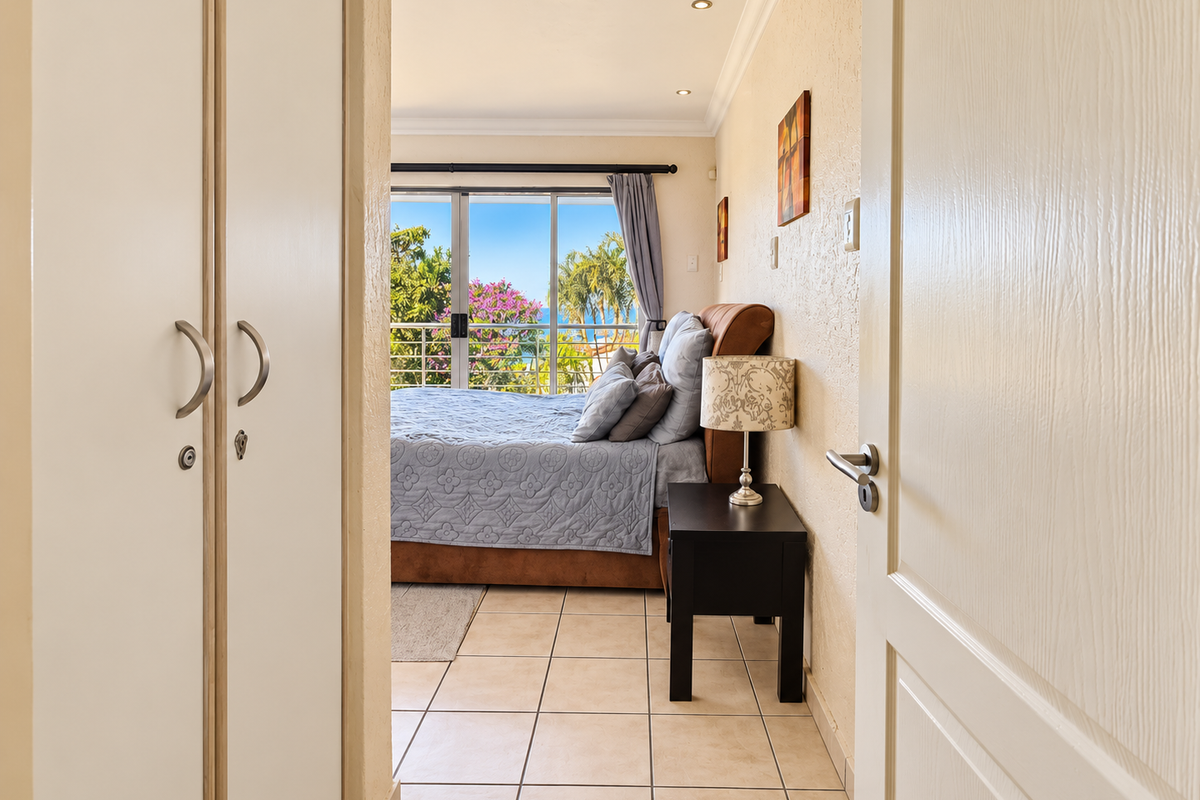 A bright bedroom featuring tiled floors, built-in cupboards, and a sliding glass door that opens to a balcony with scenic views.