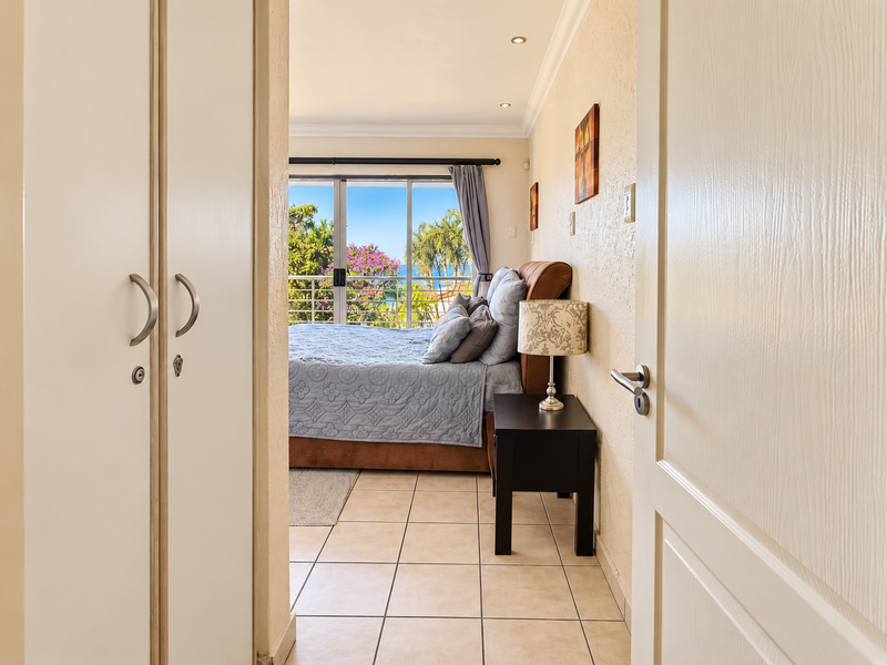 A bright bedroom featuring tiled floors, built-in cupboards, and a sliding glass door that opens to a balcony with scenic views.