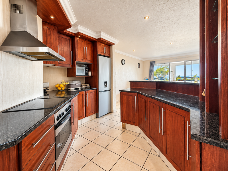 A well-maintained kitchen featuring rich wooden cabinetry, dark granite countertops, stainless steel appliances, and a breakfast bar overlooking the living area.