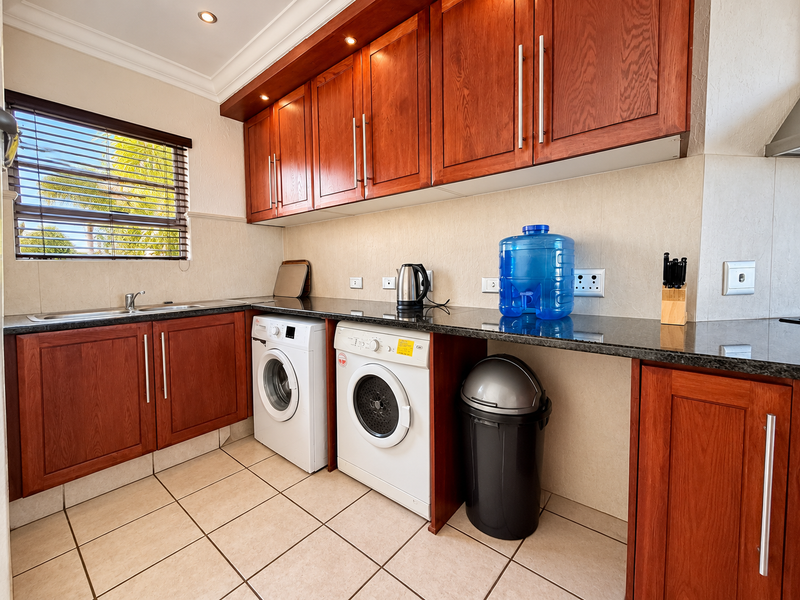 A functional laundry room featuring warm-toned wooden cabinetry, granite countertops, tiled flooring, and integrated space for laundry appliances.